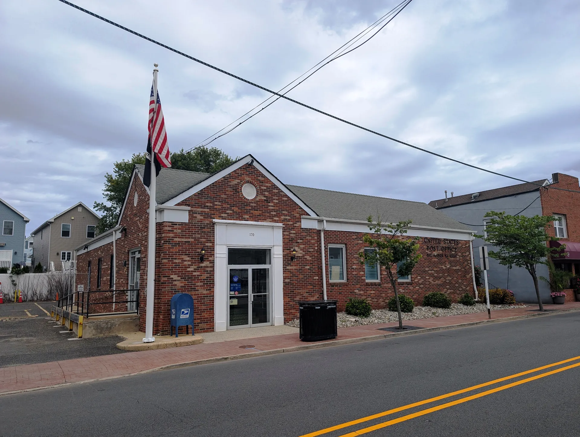The Highlands post office is a brick building with white trim, a flagpole and a blue mailbox at the curb.