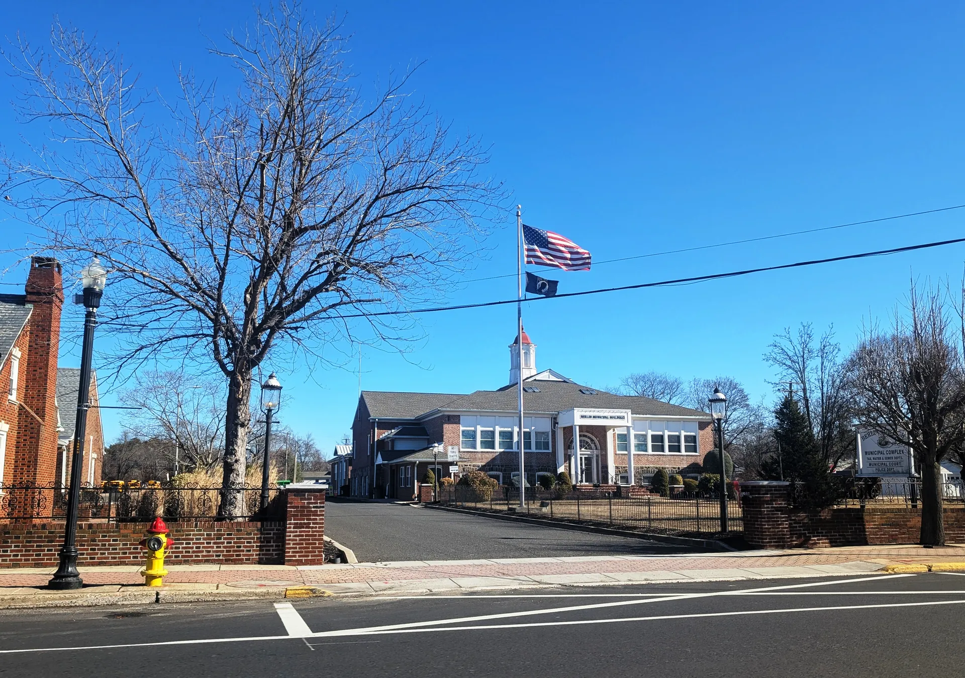 The Berlin Borough municipal building is a low brick structure with a flagpole, set back on a corner lot under bare winter trees.