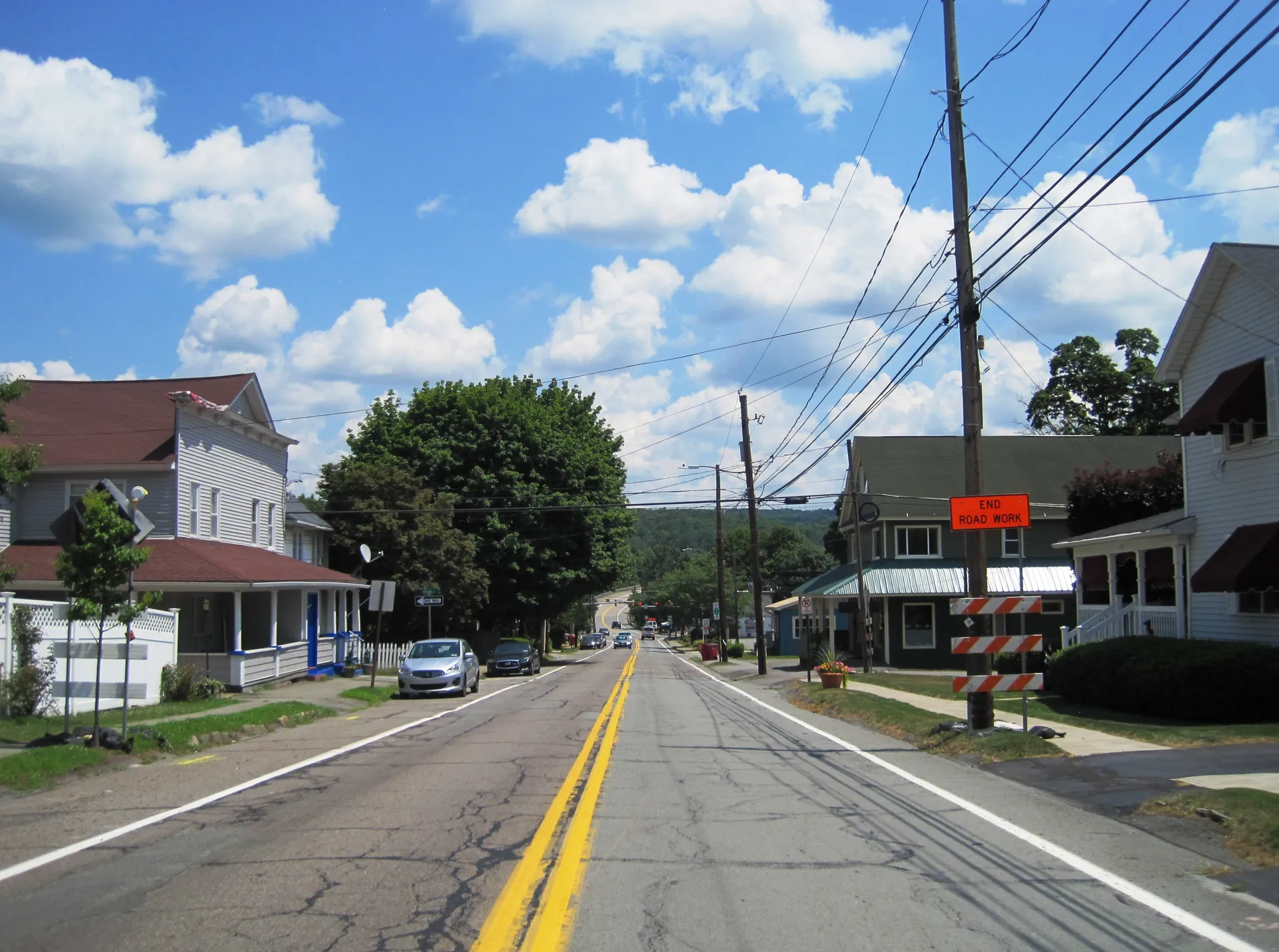 Rushbrook Street (Route 107) heads east through Jermyn past porches, a shop sign and a hillside of trees.