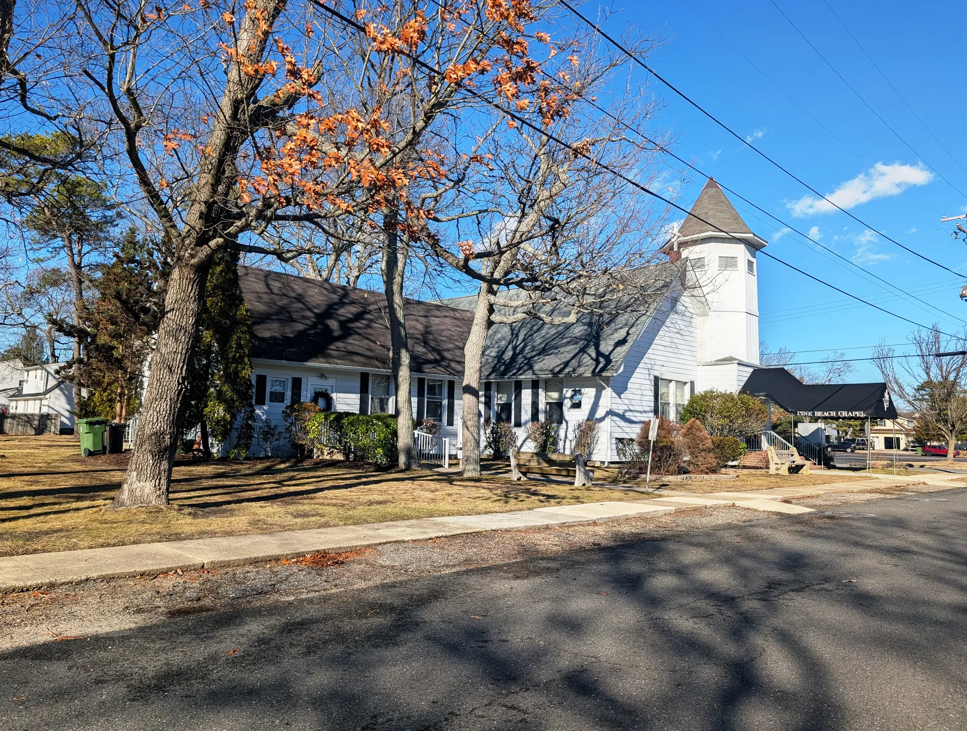 Pine Beach Chapel is a white-trimmed church with a round belfry, glimpsed through an oak with lingering orange leaves.