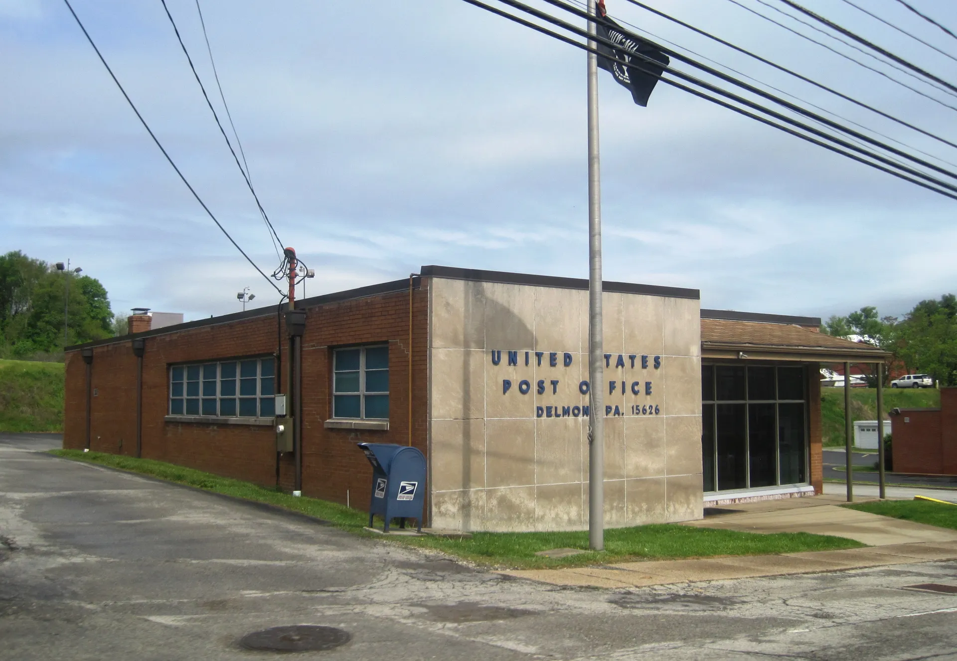 The Delmont post office is a brick building with a stone-faced entry bearing its name, beside a blue mailbox and flagpole.