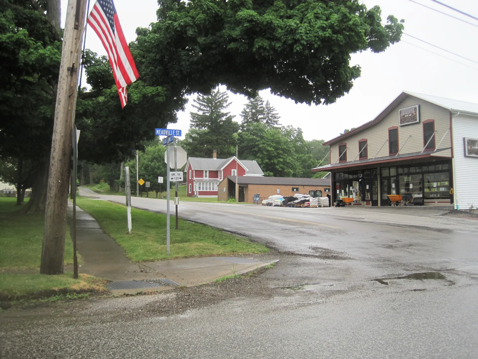East Crane Street in Cranesville leads past a flag, the borough post office and a red hardware store from Meadville Street.