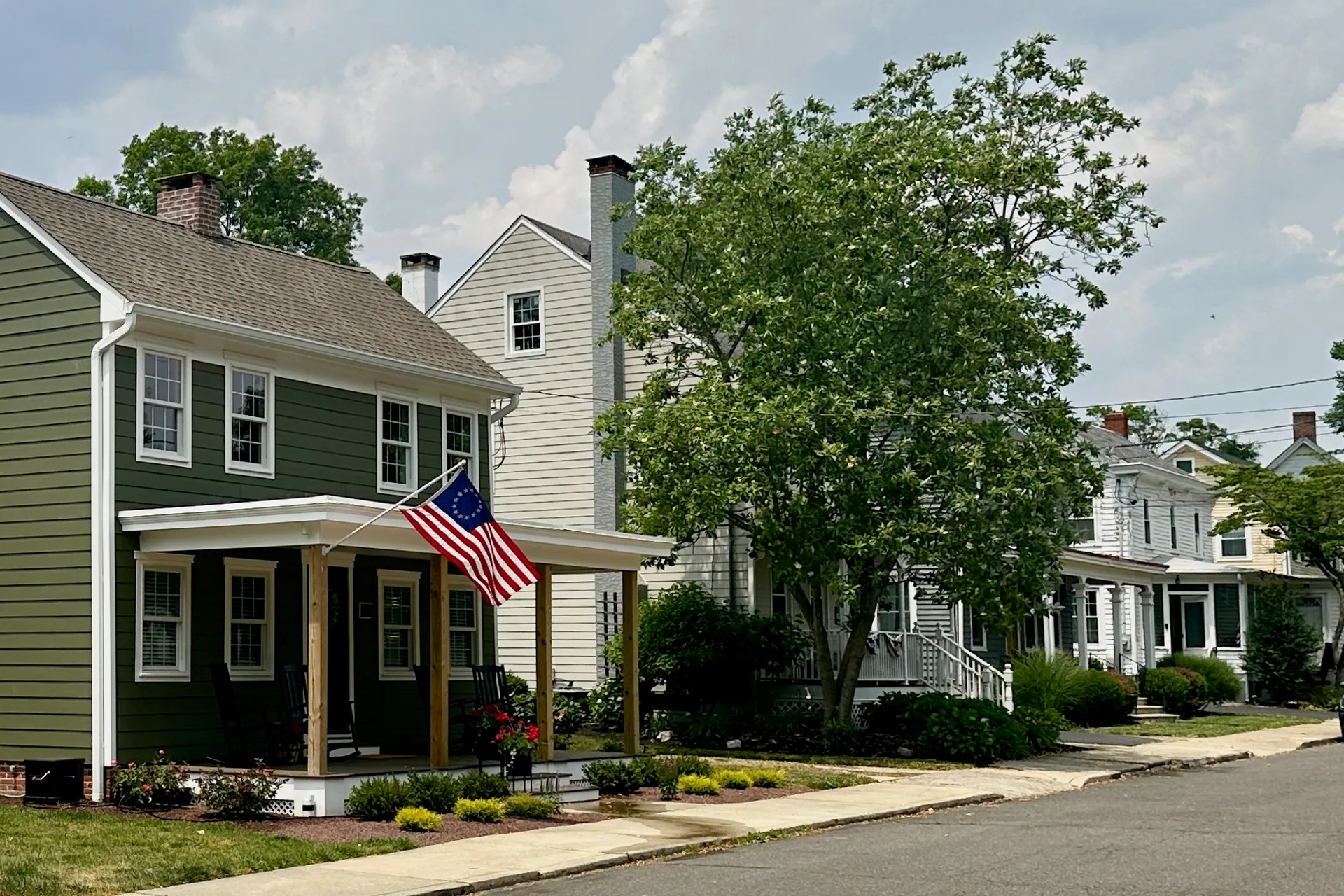 Looking along Church Street in Crosswicks, a green two-story house with an American flag on its porch sits beside a white clapboard neighbor.