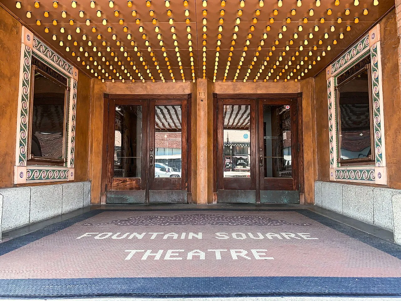 Decorative entrance lights, wooden doors and the Fountain Square Theatre name in the tiled pavement, photographed in July 2019.