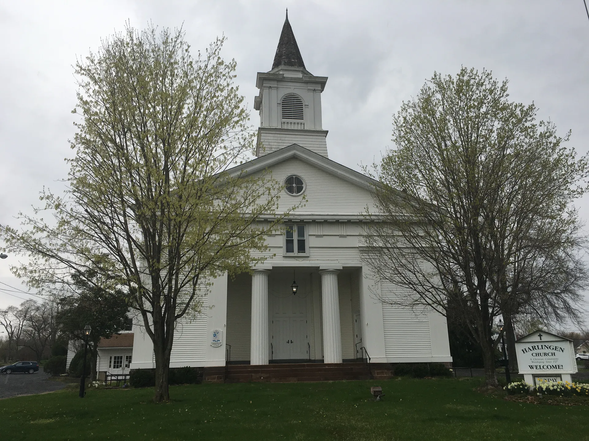 Harlingen Church is a white clapboard church with a columned front and a square clock tower among green trees.