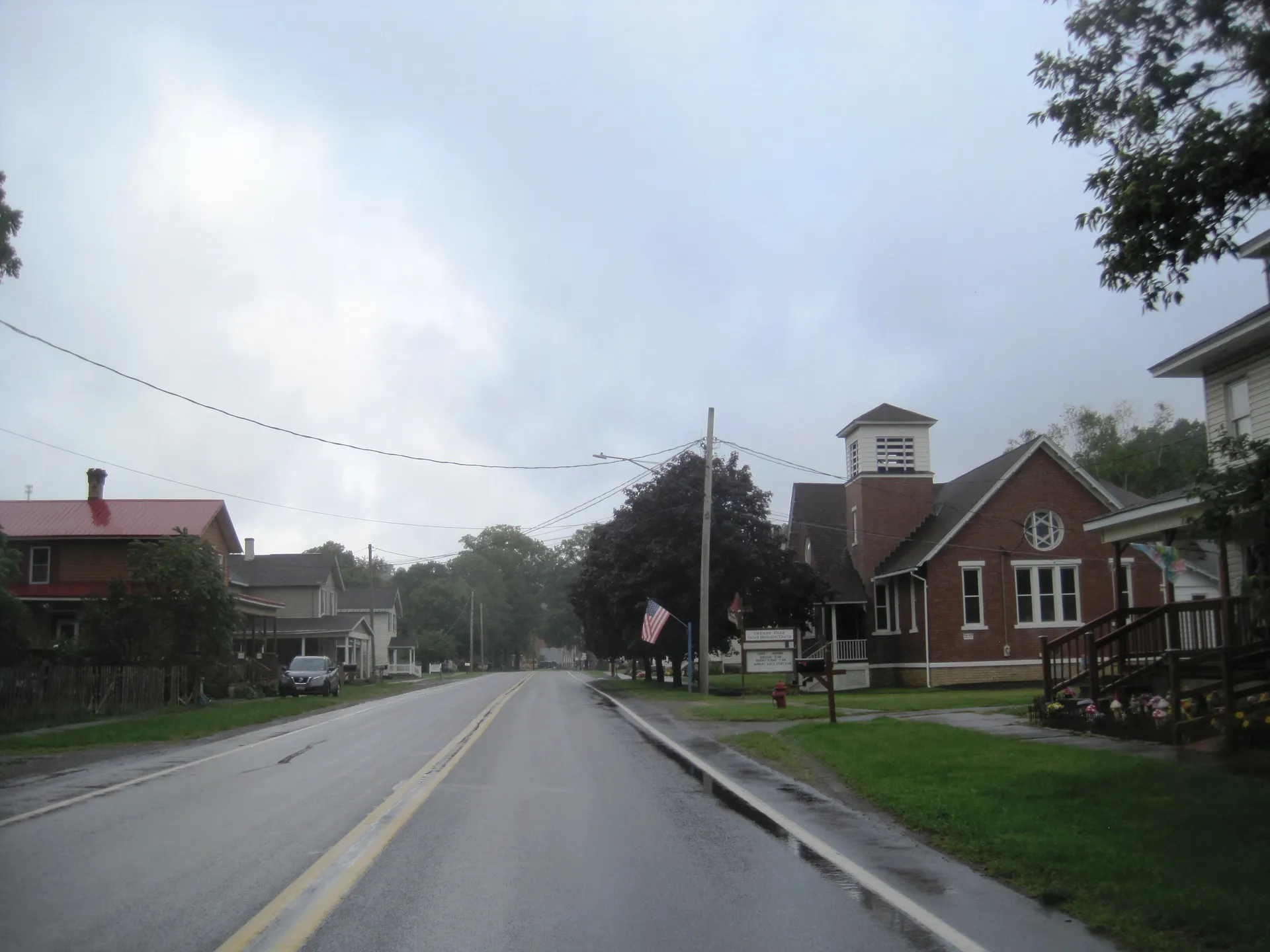 South Main Street (U.S. Route 219) enters Cherry Tree past a red-brick church and homes on a rainy day.