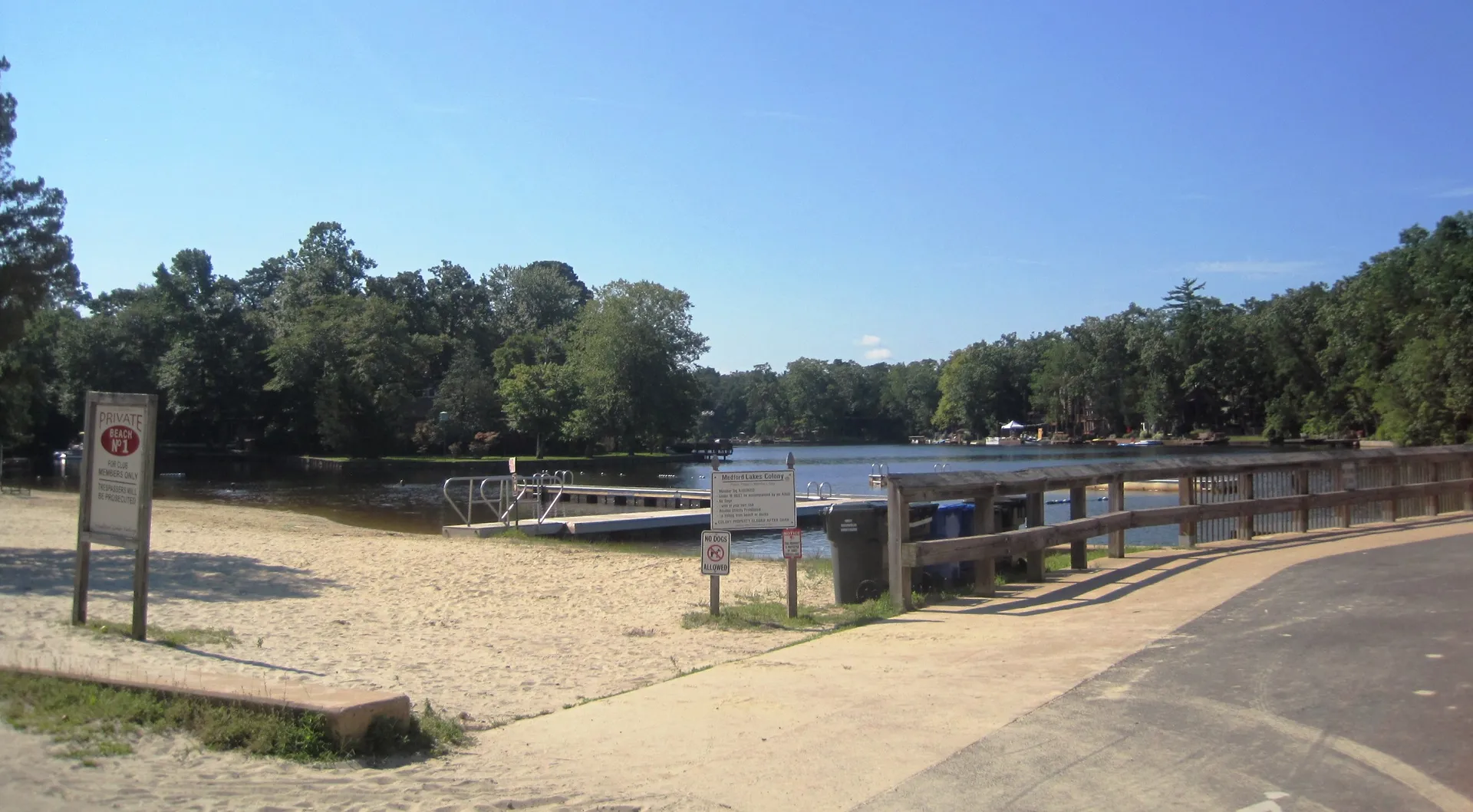 A sandy beach with lifeguard stands and a small dock edges the lake in Medford Lakes on a clear day.
