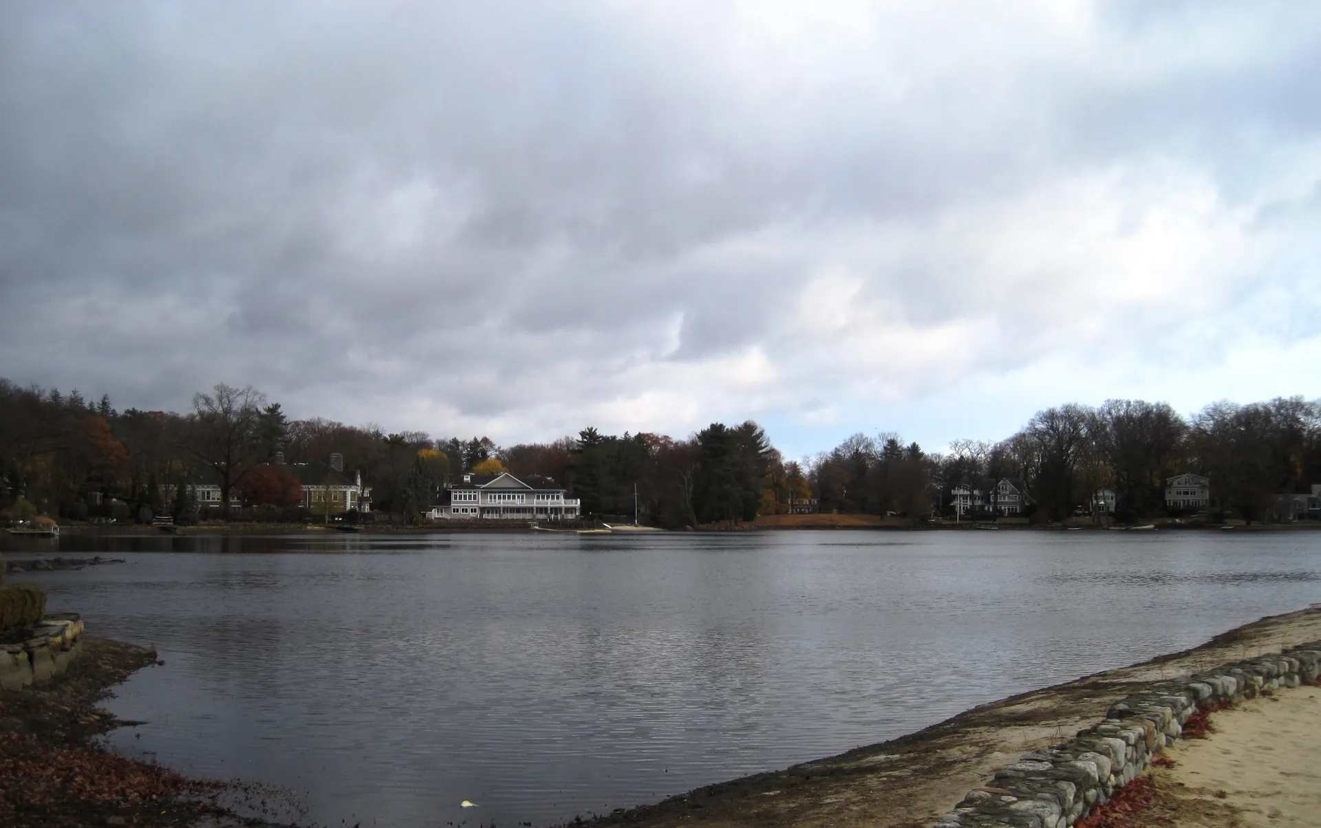 Looking north across Mountain Lake in Mountain Lakes, the gray water stretches to a wooded shoreline and houses.