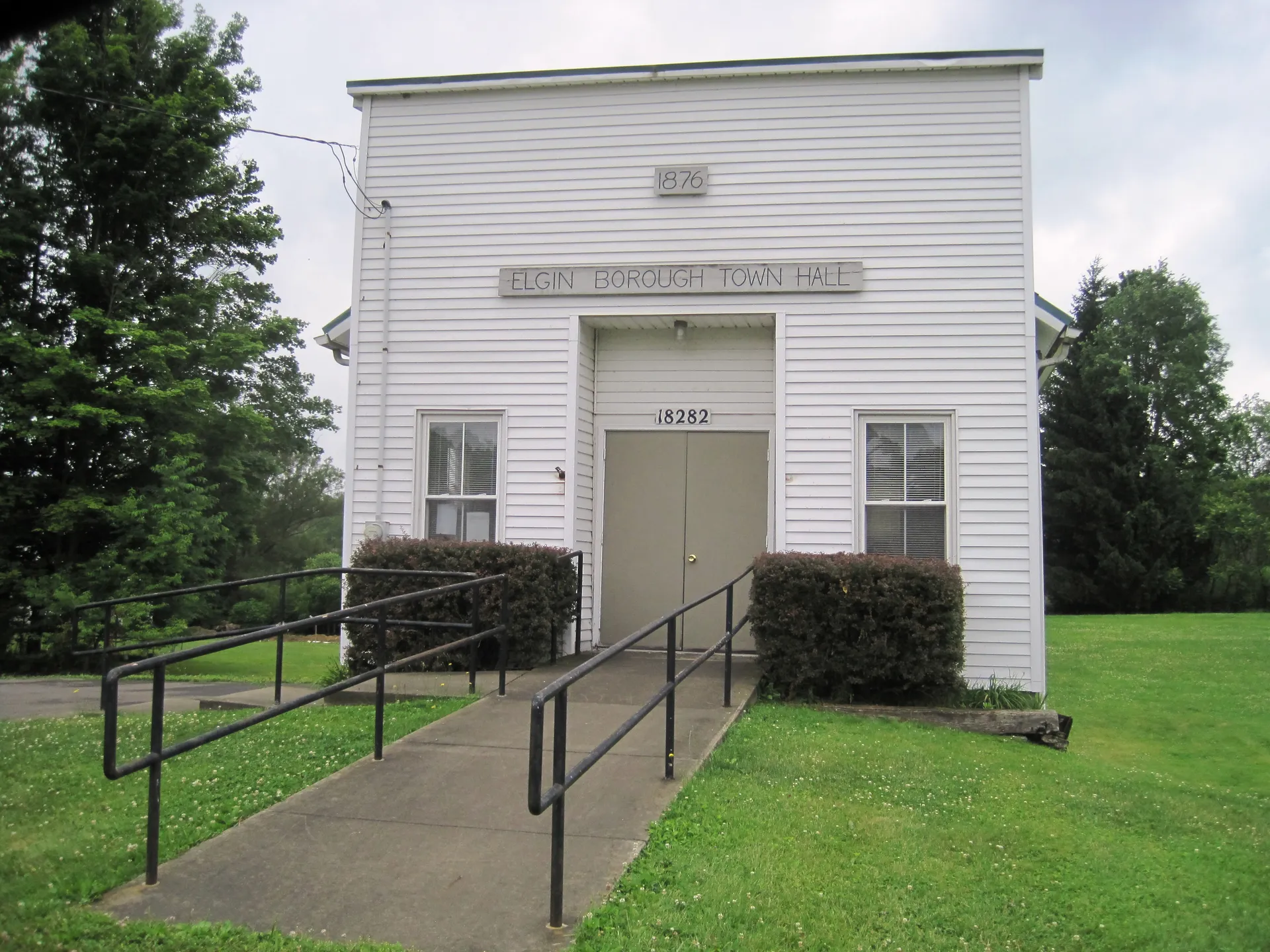 Elgin's borough hall is a white clapboard building with a central door, handrails and trimmed shrubs along Main Street.