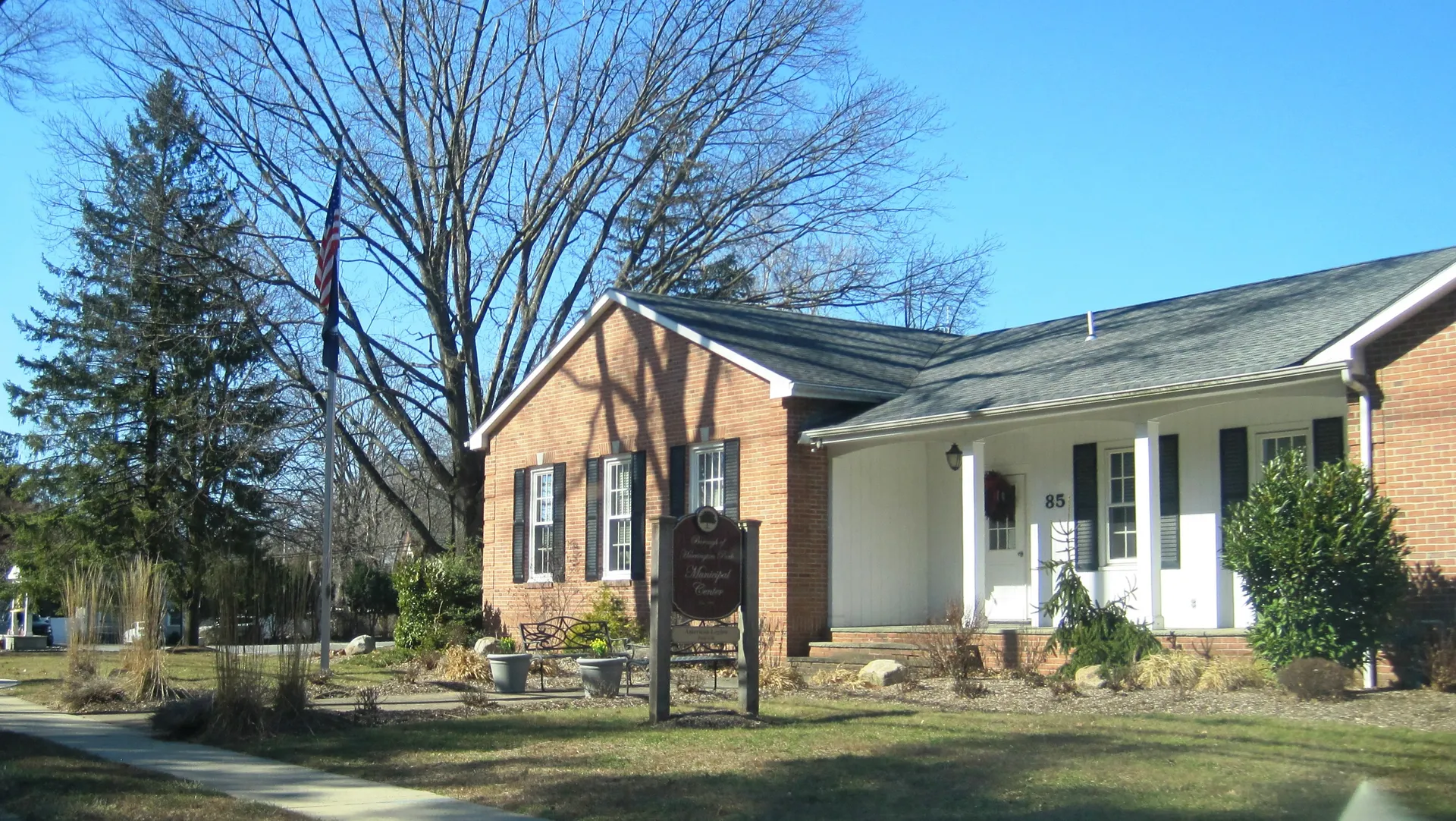 The Harrington Park municipal building is a tan brick building with a white columned porch and a sign on the lawn.