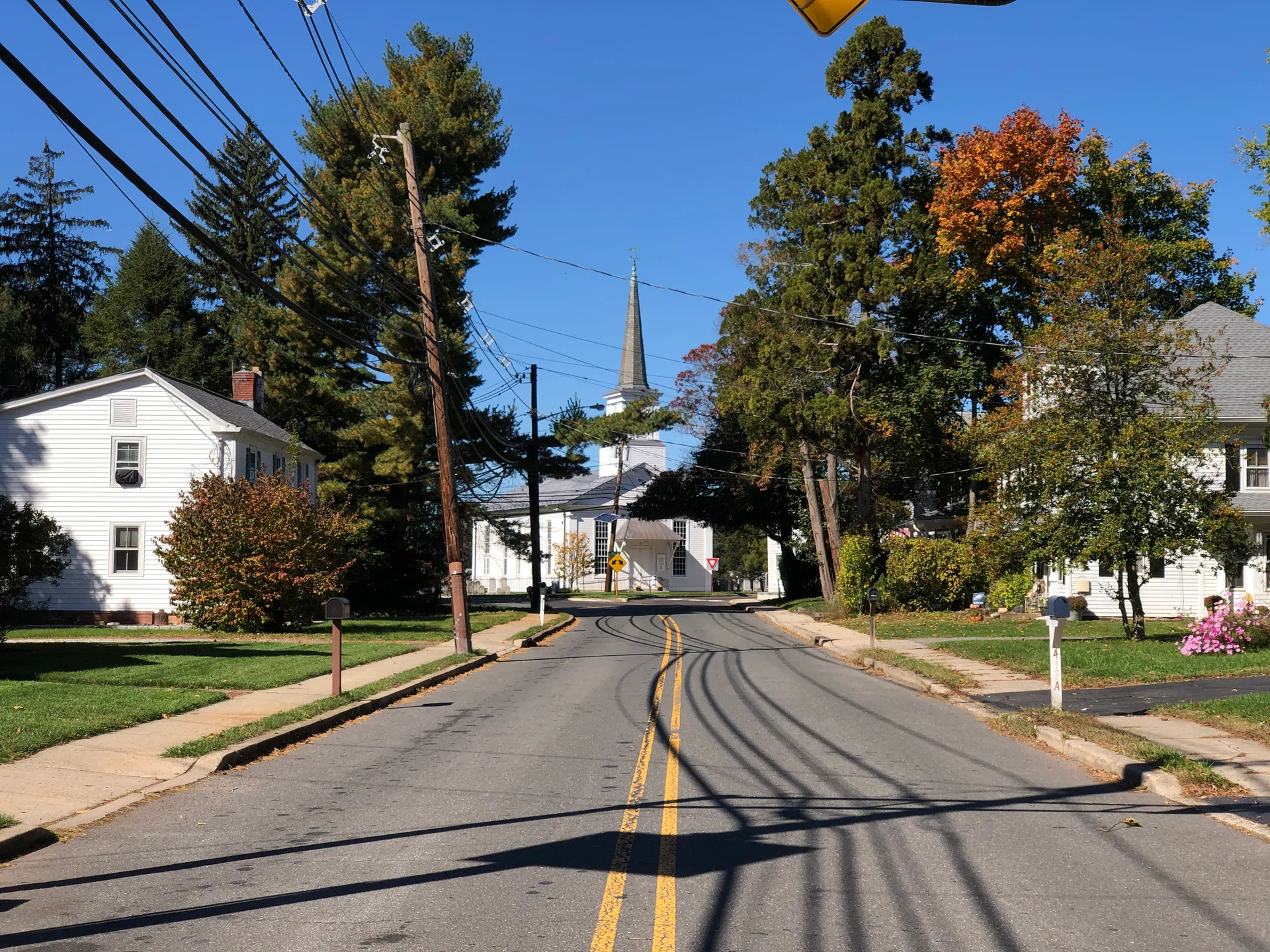 Village Road in Dutch Neck curves past houses and autumn trees toward a white church steeple in the distance.