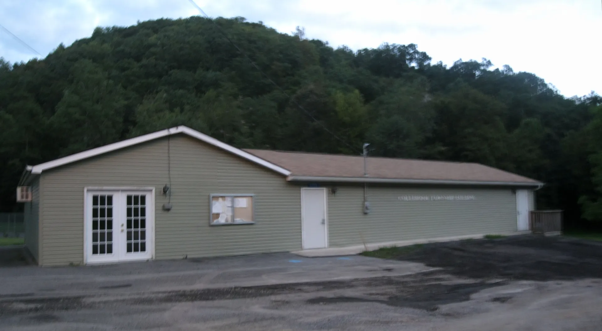 Colebrook Township's municipal building in the village of Farrandsville is a tan-sided structure beneath a steep wooded hillside.