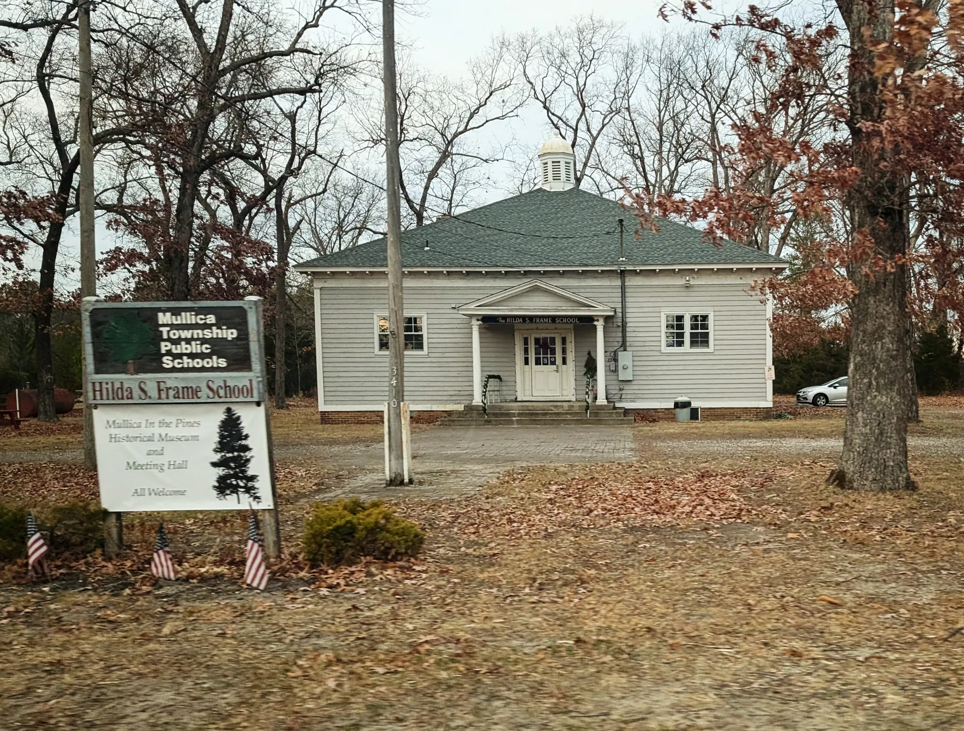The Hilda S. Frame School in Nesco is a white building with a hipped roof, a flagpole and a stone sign in front.