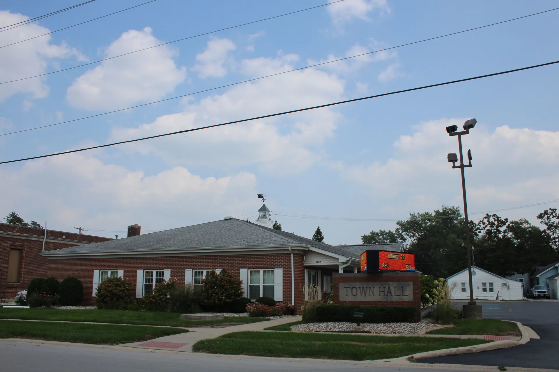 In Crete, the red brick township building with a white cupola sits behind landscaped beds and a lawn edged by a walkway.