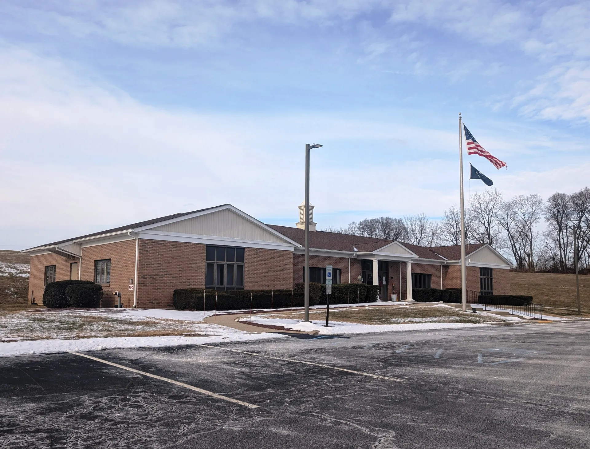 The Harmony Township municipal building is a long low brick building with a flagpole beside a snowy parking lot.