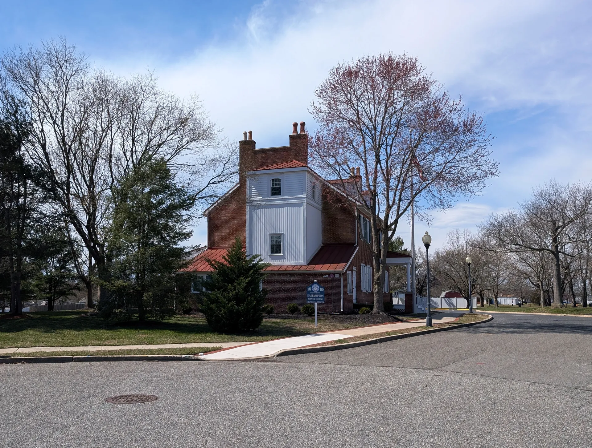 The Manor House in Eastampton Township is a red brick building with a white center bay, set beside a lawn and blossoming trees.