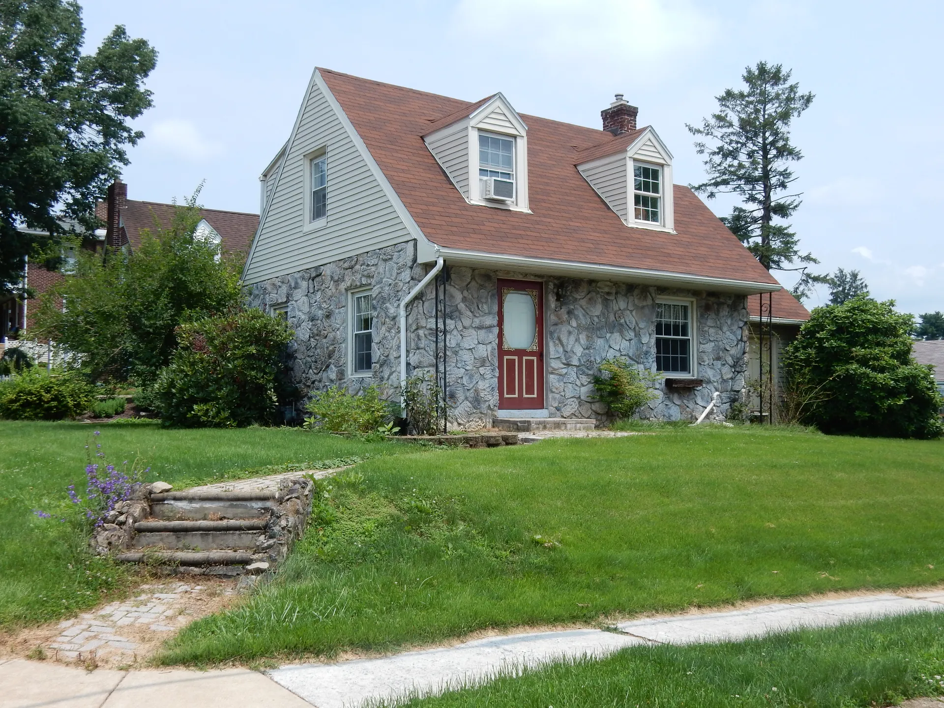 A stone-faced Cape Cod house with dormers sits above a sloping lawn at Lacrosse and Milford avenues in Kenhorst.