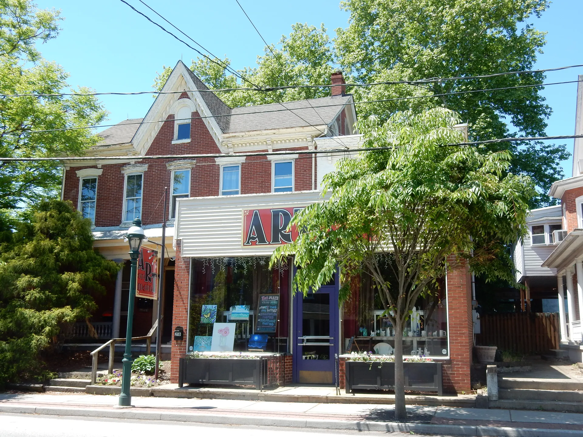 A brick storefront housing the ART on Main studio at 218 Main Street in East Greenville is decorated with flags and planters.
