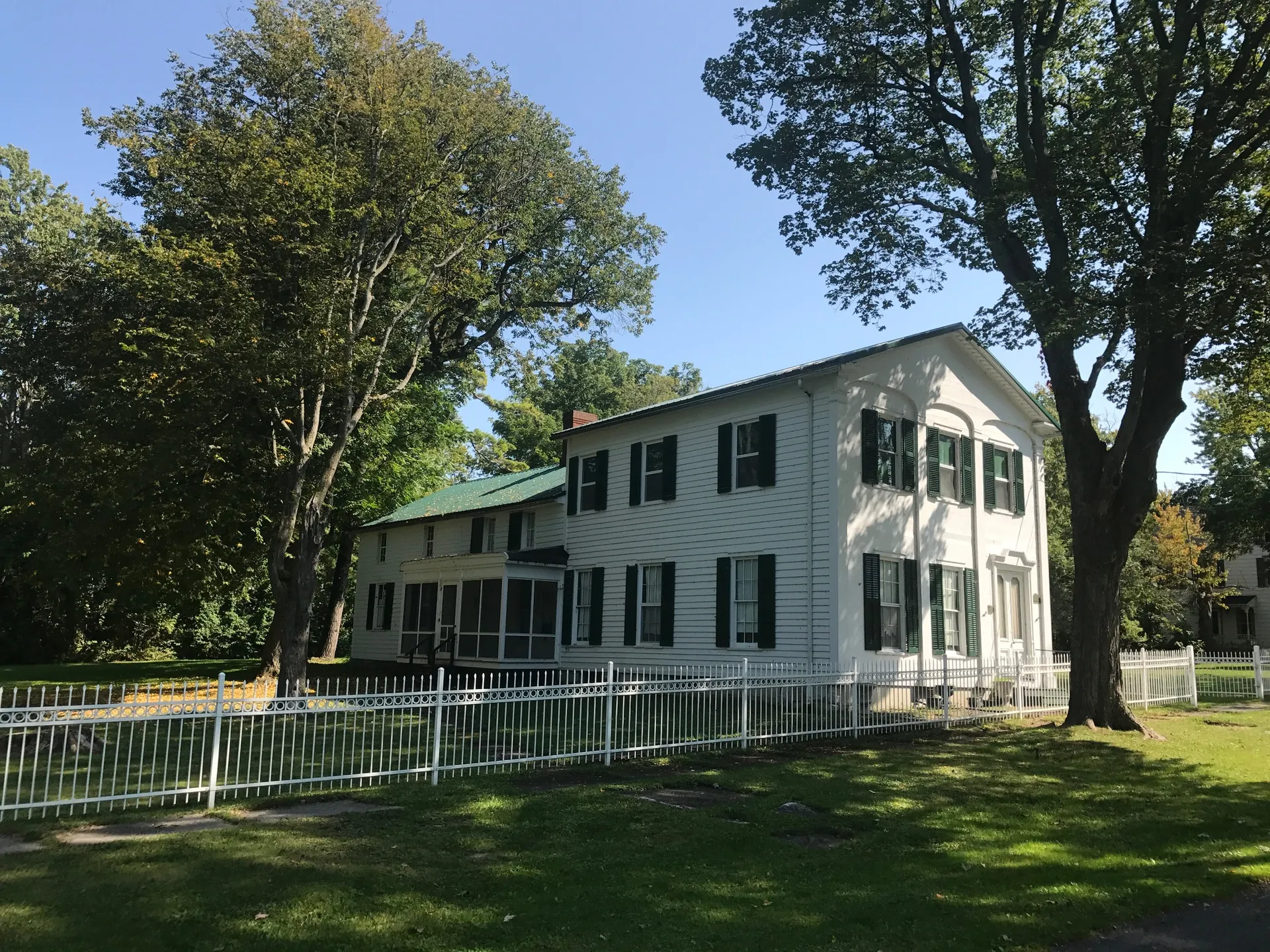 Historic white Otis Starkey House among trees in Cape Vincent, New York.